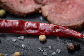 Slices of Grass Fed Corn Roast Beef garnished with dried Red Chile De Arbol Pepper and Rainbow  Peppercorns on natural black stone background.