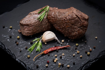 Grass Fed Corn Roast Beef garnished with Fresh Rosemary, dried Red Chile Pepper, Garlic and Rainbow  Peppercorns on natural black stone background.