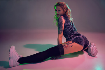 beautiful caucasian blonde girl in velour blue booty shorts and black stockings does stretching on pink background