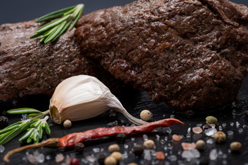 Grass Fed Corn Roast Beef garnished with Fresh Rosemary, dried Red Chile Pepper, Garlic and Rainbow  Peppercorns on natural black stone background.