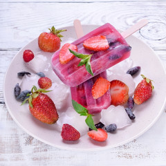 Berry popsicles with pieces of strawberry and honeysuckle on the white plate