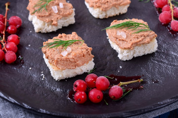 Canape with foie gras on the black plate. Red currant berries around