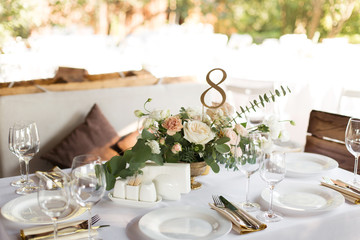 Wedding table setting decorated with fresh flowers in a brass vase. Wedding floristry. Banquet table for guests outdoors with a view of green nature. Bouquet with roses, eustoma and eucalyptus leaves