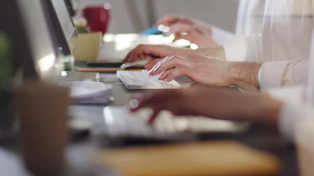 Side close up view of employees typing on their computers using keyboards in light modern office. Profession concept, modern technologies, working hard. Making money, workaholics