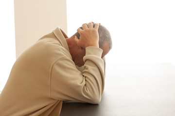 A man is sitting alone at a table head buried in his hands. A sign of grief, sadness or...