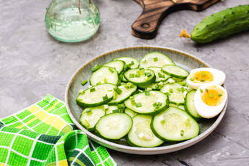 Ready-to-eat fresh cucumber salad, boiled chicken egg and green onions on a plate on the table