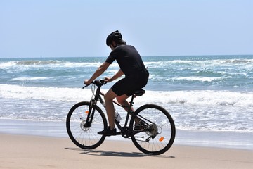 Fototapeta na wymiar Cyclist riding in the edge of water on a deserted beach