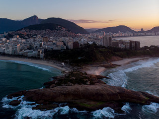 Rock formation on the coast of Rio de Janeiro locally known as Arpoador, harpooner with in the background the wider cityscape with the Corcovado mountain against an orange sunrise sky