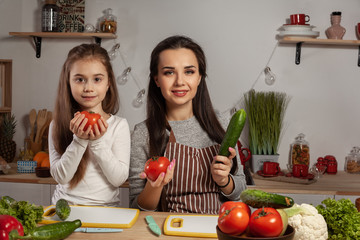Mother and her daughter are making a vegetable salad and having fun at the kitchen.