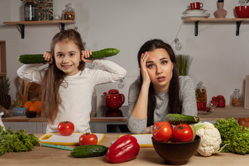 Mother and her daughter are making a vegetable salad and having fun at the kitchen.