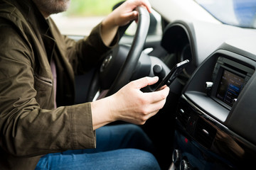 Car interior. Depicted a man behind the wheel. He holds the phone in his hand. Selective focus.
