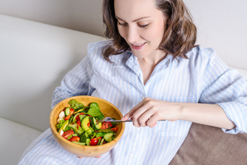 Young smiling woman with blue shirt eating fresh vegetable salad