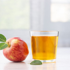 Glass of apple juice and ripe red apple with leaves on a table.