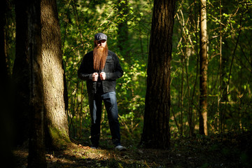 Obraz premium Bearded man. Portrait of an serious caucasian adult man with a very long beard in a cap on a sunny day outside in the dark forest.