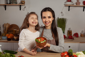 Mother and her daughter are making a vegetable salad and having fun at the kitchen.