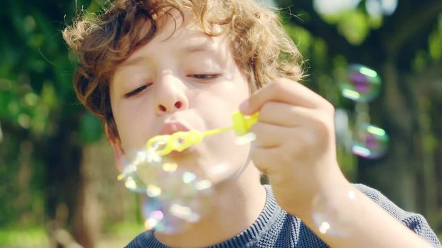 close-up shot of a 10 year-old italian boy having fun blowing bubbles outdoors in a park