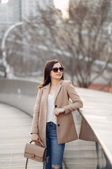 Fototapeta premium Beautiful girl in a park. Stylish brunette in a brown jacket. Lady in a sunglasses