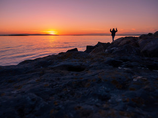 Silhouette of a teenager, hands in the air,  sunset over ocean, concept: emotion, excitement.