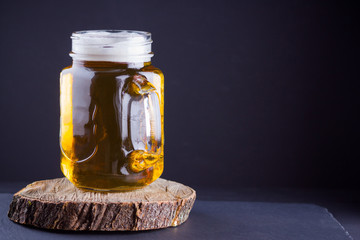 Beer with foam in mason jar on a dark background. A glass of light beer on a wooden stand. Low alcohol drink on slate board. Copy space