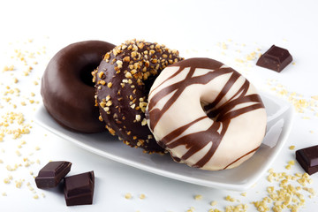 Set of delicious fresh donuts with pieces of chocolate and nut crumb on white background. Appetizing tasty glazed donuts with chocolate, white chocolate and walnut pieces served on plate.