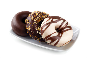 Set of fresh and delicious donuts served on a plate isolated on white background. Appetizing and tasty donuts glazed with chocolate, white chocolate and walnut pieces served on a plate.