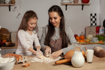 Mother and her daughter are baking a bread and having fun at the kitchen.