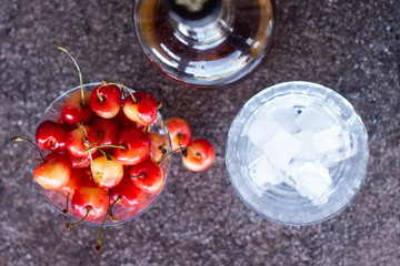 Yellow sweet cherries in a whiskey glass, ice cubes and a bottle of whiskey against a stone background. A refreshing cold cocktail at the base of the whiskey.