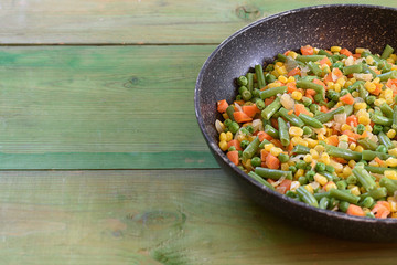 Mix on vegetables fried in a wok. Green peas, carrot, corn , green beans, onion in the pan on wooden background.Copy space.Healthy food concept.