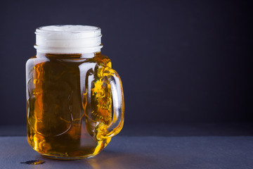 Beer with foam in mason jar on a dark background. A glass of light beer. Low alcohol drink on slate board. Copy space