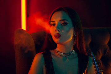 Sexy brunette model is smoking a hookah exhaling a smoke at a luxury night club.