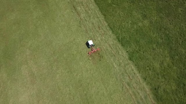 Tractor raking grass in an aerial view. Tracking shot of farmer doing field work with dry hay on a sunny day on meadow.