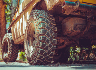 Big and dirty tires of an off-road car sitting on the street – Yellow monster truck with huge rubber wheels with a rough and detailed surface © madrolly