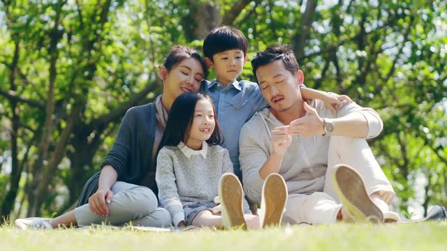 asian family with two children sitting on grass outdoors in a park talking chatting