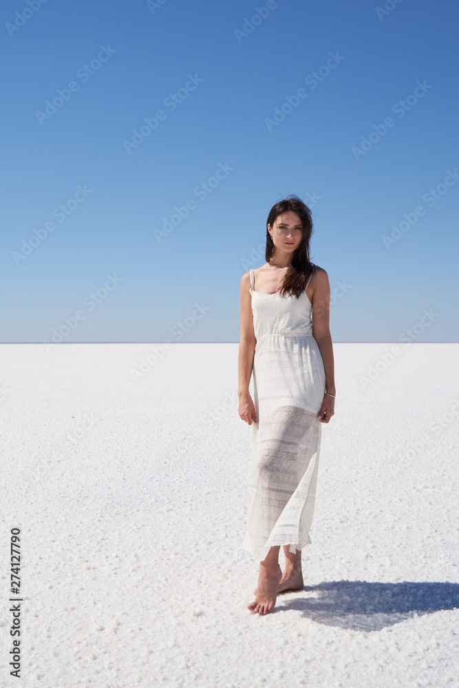 Wall mural dark-haired girl in a white dress posing on the dried up salt lake elton in the volgograd region in 