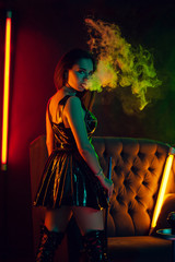 Sexy brunette model is smoking a hookah exhaling a smoke at a luxury night club.