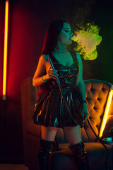 Sexy brunette model is smoking a hookah exhaling a smoke at a luxury night club.