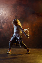 Photo of dancing long-haired blonde woman in torn blue jeans on brown background