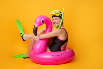 Photo of girl swimmer in black swimsuit in flippers with life ring in form of flamingos on orange background © Sergey Mironov