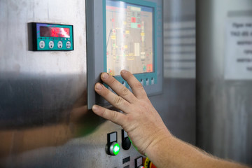 Worker clicks on touch screen of control panel on industrial equipment of beverage plant or factory