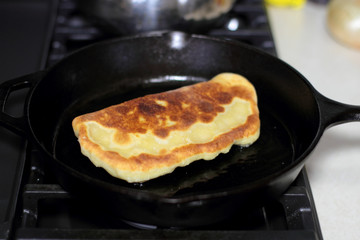 Pan fried calzone cooking in a cast iron skillet on a stove.