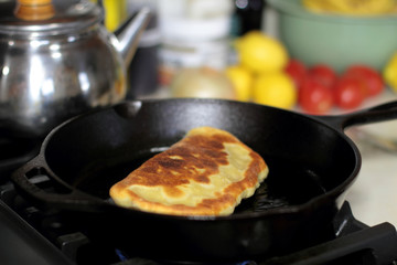 Pan fried calzone cooking in a cast iron skillet on a stove.