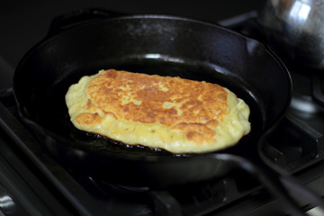 Pan fried calzone cooking in a cast iron skillet on a stove.