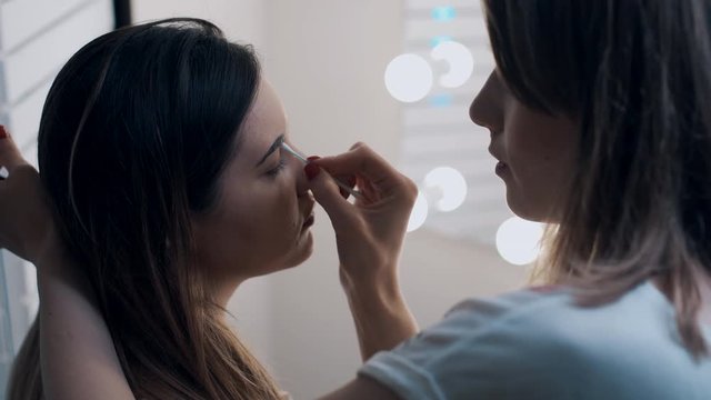 make up artist tweezing eyebrows of young beautiful female