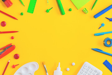 Assorted office and school red green blue and white stationery on bright yellow background. Flat lay with copy space for back to school or education and craft concept. Border or frame