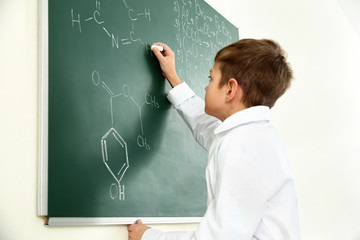 Schoolboy writing formula on blackboard in chemistry class