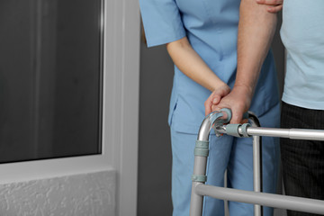Nurse assisting senior patient with walker in hospital, closeup