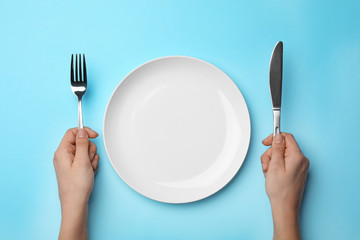 Woman with fork, knife and empty plate on color background, top view