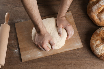 Male baker preparing bread dough at wooden table, above view