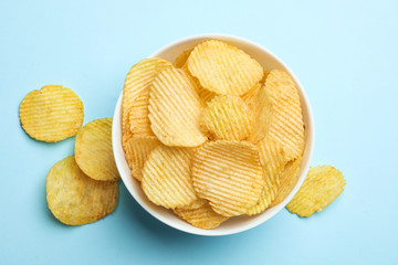 Delicious crispy potato chips in bowl on color background, top view