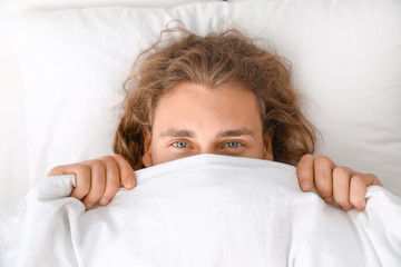 Young man covering his face with blanket while lying on pillow, top view. Bedtime